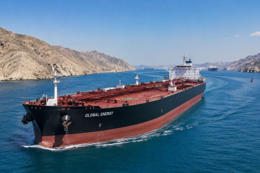 Commercial oil tanker navigating through the narrow waters of the Strait of Hormuz under a clear sky, representing global energy trade pathways.