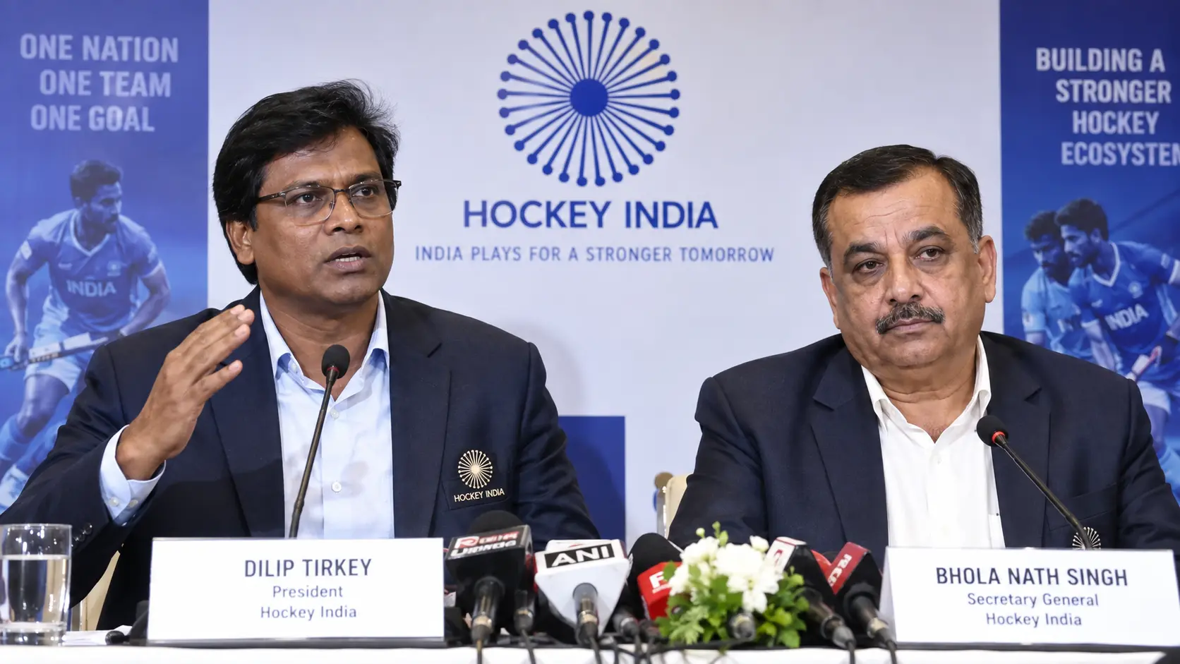 Dilip Tirkey, President of Hockey India, standing beside Secretary General Bhola Nath Singh at a national sports governance press brief in New Delhi.